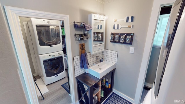 laundry area with stacked washer / drying machine, a sink, baseboards, and wood finished floors