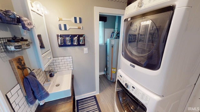 laundry room featuring stacked washer and clothes dryer, gas water heater, wood finished floors, laundry area, and baseboards