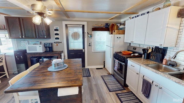 kitchen featuring stainless steel stove, white microwave, light wood-style floors, white cabinets, and a sink