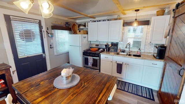 kitchen with a barn door, a sink, white cabinets, freestanding refrigerator, and stainless steel range with gas stovetop