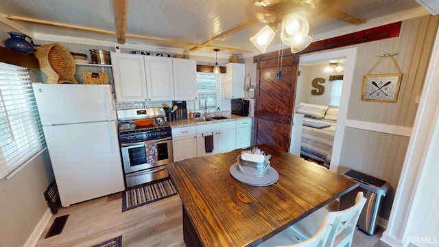 kitchen with gas range, a sink, freestanding refrigerator, and white cabinetry