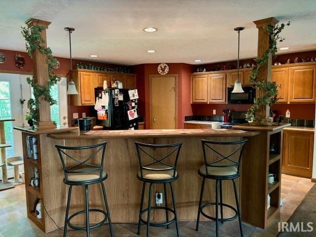 kitchen featuring black appliances, a breakfast bar area, a center island, and decorative light fixtures