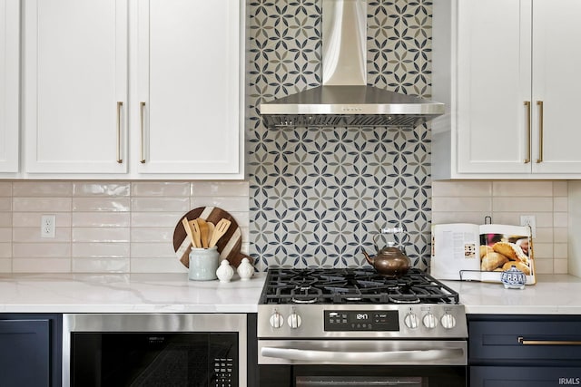 kitchen featuring white cabinetry, backsplash, light stone counters, stainless steel gas range oven, and wall chimney exhaust hood