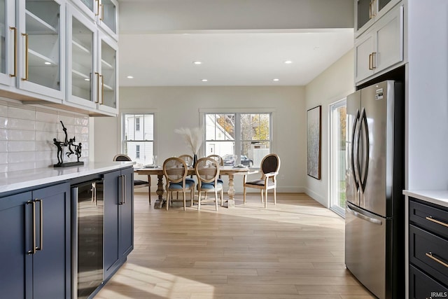 kitchen with stainless steel fridge, backsplash, wine cooler, white cabinets, and light wood-type flooring