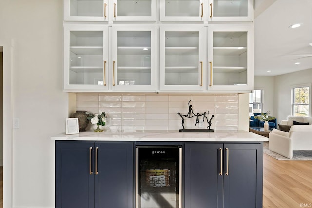 bar with blue cabinetry, wine cooler, light hardwood / wood-style floors, and decorative backsplash