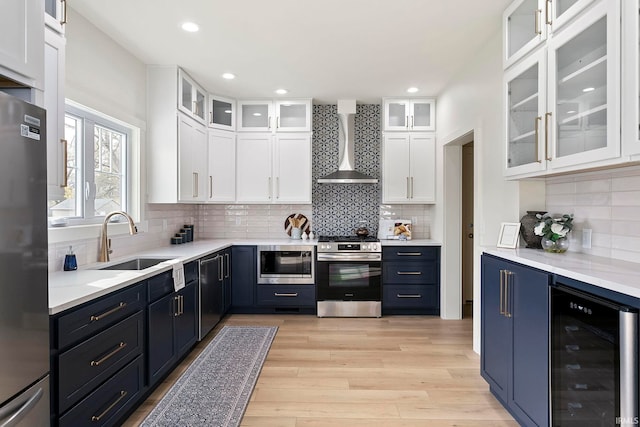 kitchen with white cabinetry, wine cooler, stainless steel appliances, wall chimney range hood, and light wood-type flooring