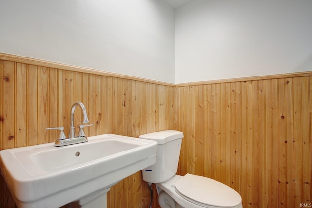 bathroom with wood walls, toilet, and sink