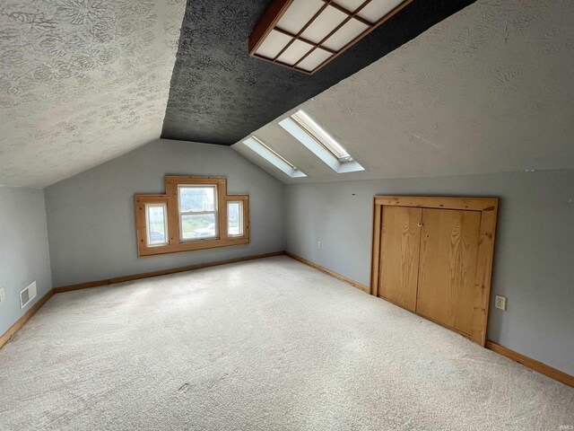 additional living space with vaulted ceiling with skylight, a textured ceiling, and carpet flooring