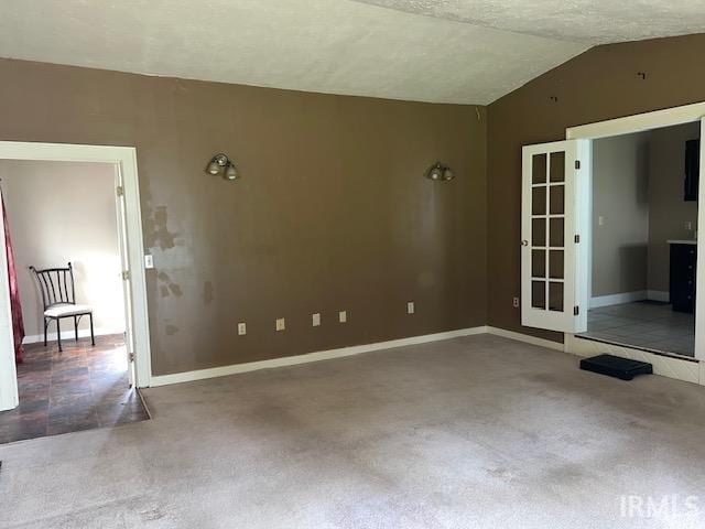 carpeted empty room featuring vaulted ceiling and a textured ceiling