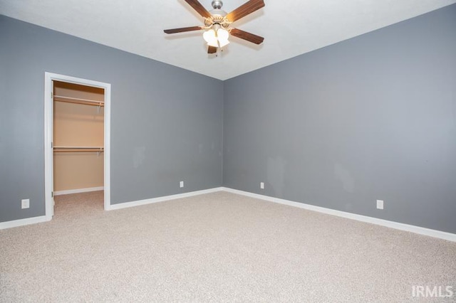 unfurnished bedroom featuring ceiling fan, a closet, light carpet, a walk in closet, and baseboards