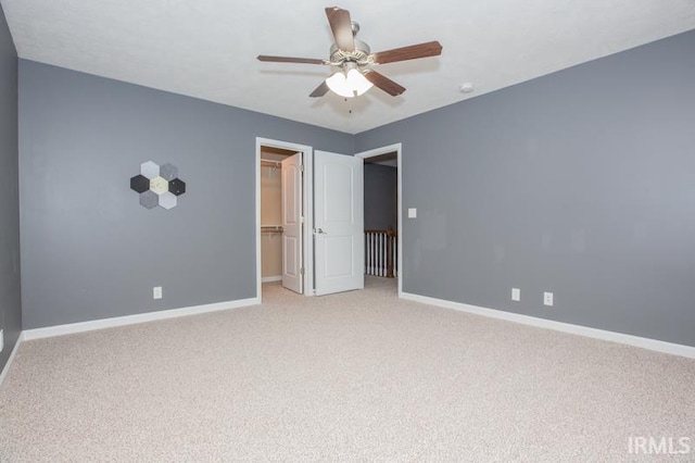 unfurnished bedroom with a closet, baseboards, a ceiling fan, a walk in closet, and light carpet