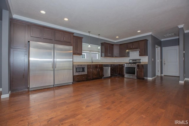 kitchen featuring dark brown cabinetry, stainless steel appliances, dark hardwood / wood-style flooring, pendant lighting, and ornamental molding