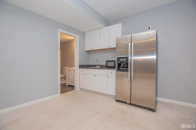 kitchen featuring stainless steel refrigerator with ice dispenser, light colored carpet, sink, and white cabinets