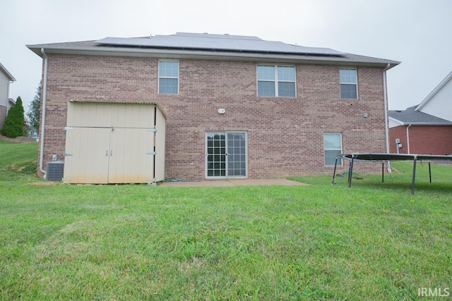 back of property featuring solar panels, a yard, a trampoline, and central air condition unit