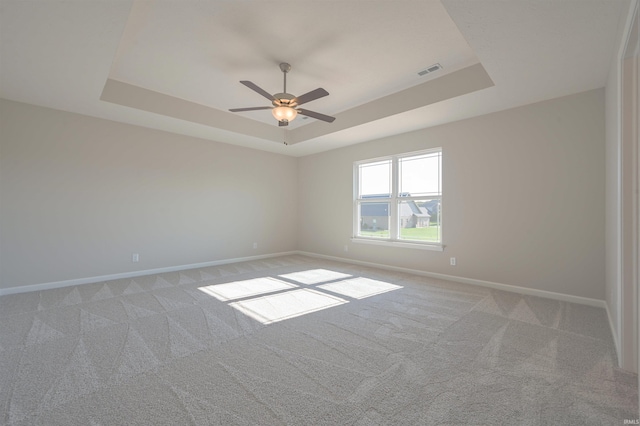 carpeted empty room featuring ceiling fan and a raised ceiling