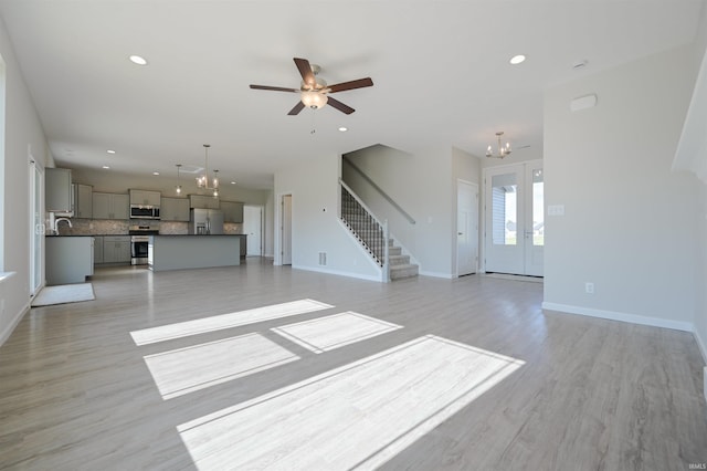 unfurnished living room with sink, light hardwood / wood-style flooring, ceiling fan with notable chandelier, and french doors