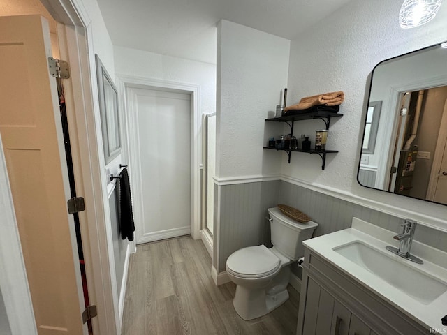 bathroom featuring a shower, wood finished floors, toilet, vanity, and wainscoting