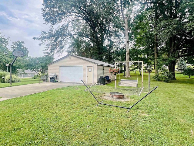 view of yard with a garage, an outbuilding, driveway, and a fire pit