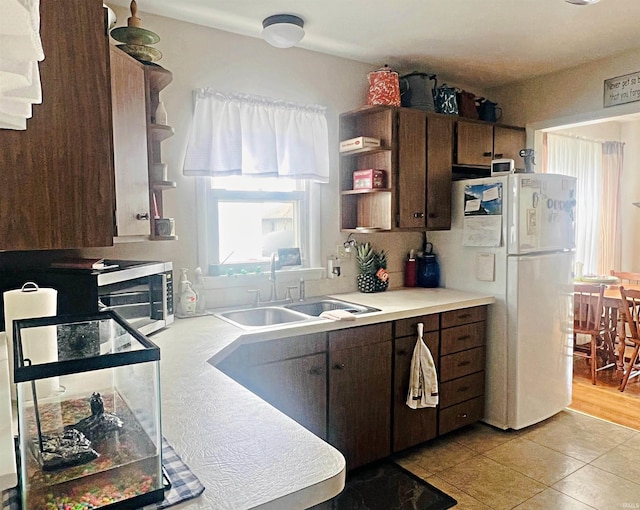 kitchen with light tile patterned floors, open shelves, light countertops, freestanding refrigerator, and a sink