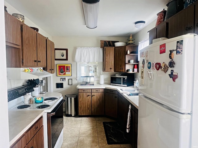 kitchen with range with electric stovetop, light countertops, stainless steel microwave, freestanding refrigerator, and exhaust hood