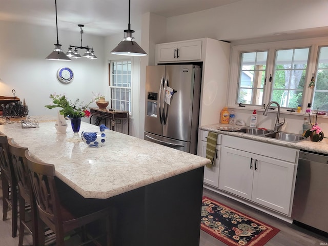 kitchen with decorative light fixtures, sink, white cabinets, a center island, and stainless steel appliances