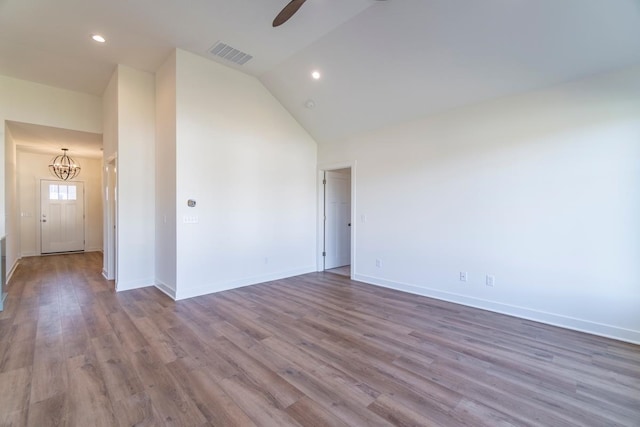 empty room with lofted ceiling, ceiling fan with notable chandelier, and hardwood / wood-style floors