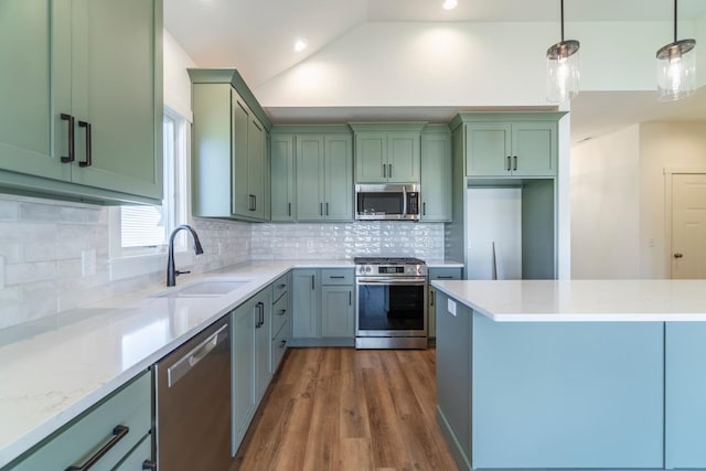 kitchen with sink, green cabinetry, hanging light fixtures, stainless steel appliances, and light stone counters