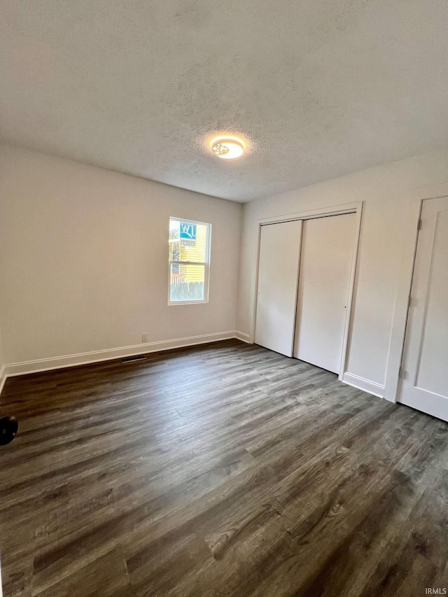 unfurnished bedroom with a textured ceiling, a closet, and dark hardwood / wood-style flooring