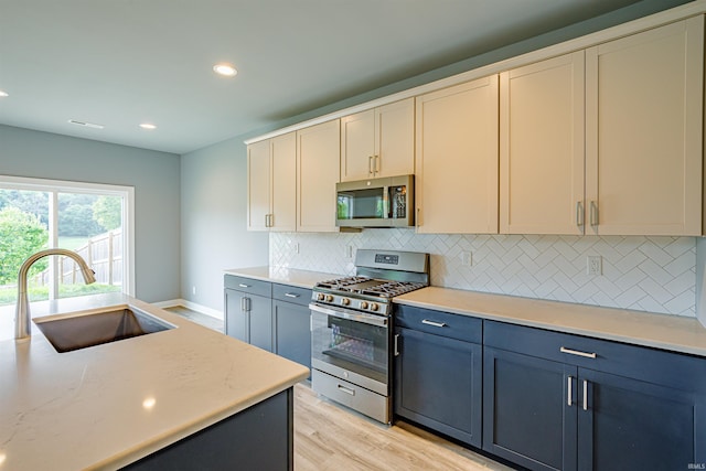 kitchen with sink, backsplash, stainless steel appliances, light stone counters, and light wood-type flooring