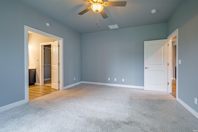 unfurnished bedroom with a walk in closet, light colored carpet, a closet, and ceiling fan