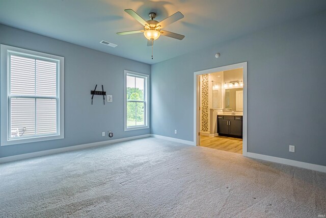 unfurnished bedroom featuring ensuite bath, light colored carpet, and ceiling fan