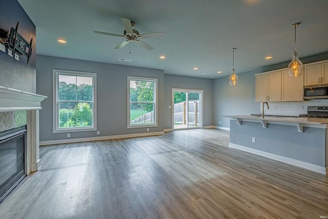 unfurnished living room with sink, a fireplace, light hardwood / wood-style floors, and ceiling fan