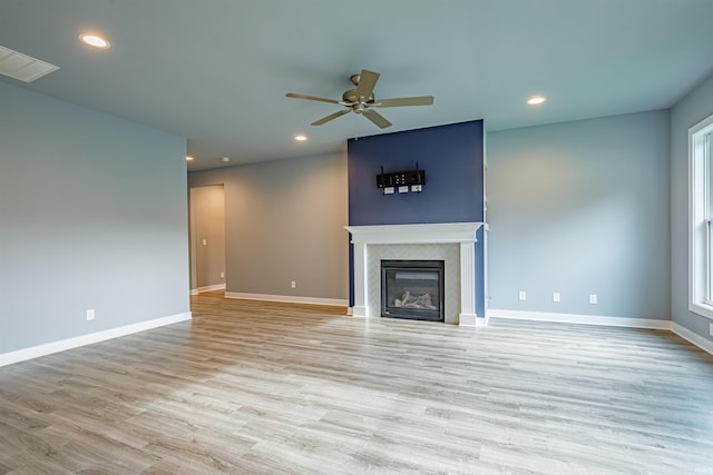 unfurnished living room with a healthy amount of sunlight, a tile fireplace, ceiling fan, and light wood-type flooring