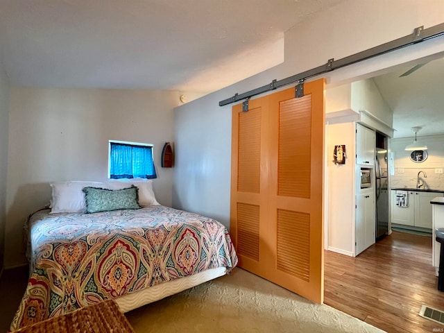 bedroom with a barn door, stainless steel refrigerator, hardwood / wood-style flooring, sink, and lofted ceiling