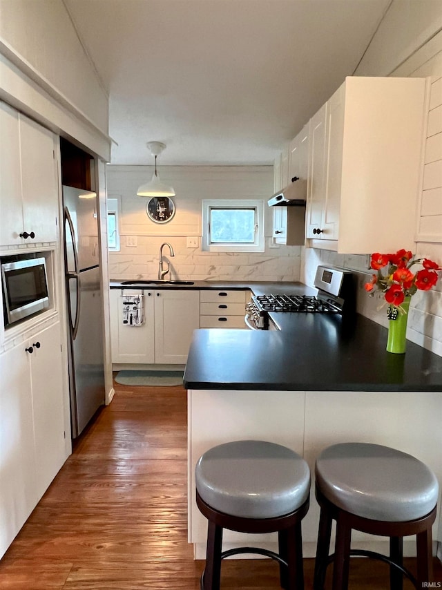 kitchen featuring appliances with stainless steel finishes, backsplash, white cabinetry, dark hardwood / wood-style floors, and kitchen peninsula