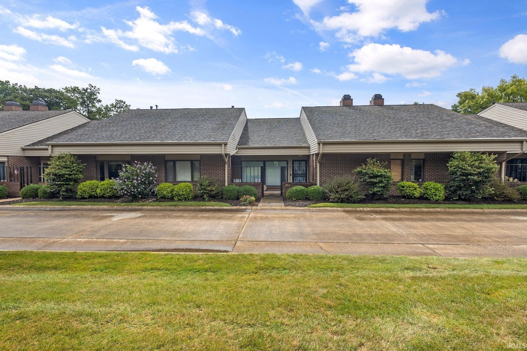 view of front of house featuring brick siding, a front yard, and a shingled roof