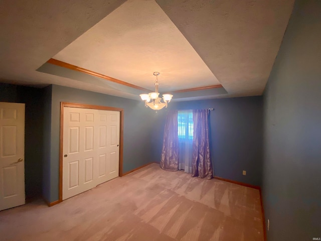 unfurnished bedroom featuring an inviting chandelier, a tray ceiling, a closet, and carpet flooring