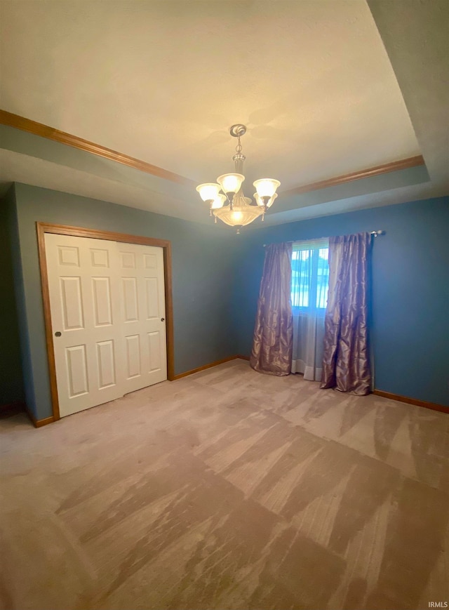 unfurnished bedroom featuring a tray ceiling, carpet flooring, a chandelier, and a closet