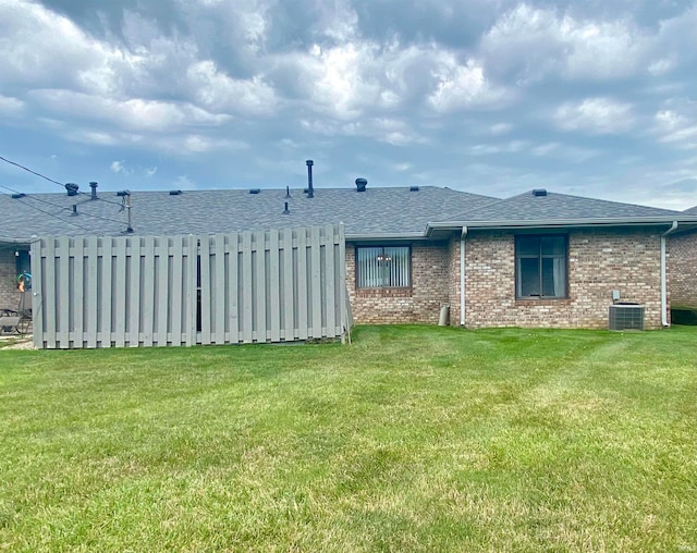 rear view of property featuring central air condition unit and a lawn