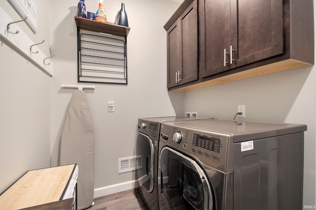 clothes washing area featuring hardwood / wood-style flooring, washer and clothes dryer, and cabinets