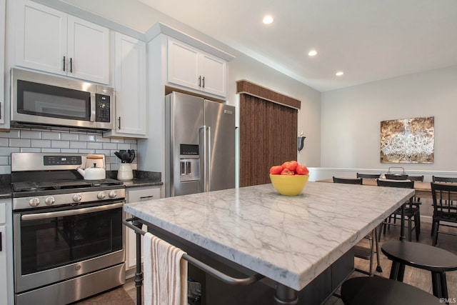 kitchen with backsplash, a center island, appliances with stainless steel finishes, light stone countertops, and white cabinetry