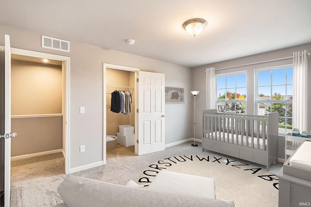 carpeted bedroom featuring a walk in closet, a closet, a crib, and ensuite bathroom