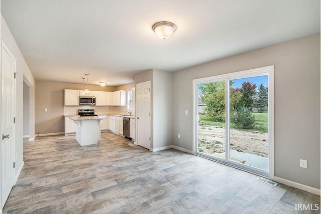 kitchen featuring hanging light fixtures, stainless steel appliances, a center island, white cabinetry, and light hardwood / wood-style floors