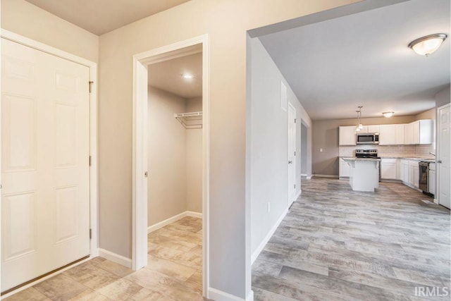 kitchen with a center island, stainless steel appliances, decorative light fixtures, white cabinets, and light hardwood / wood-style flooring