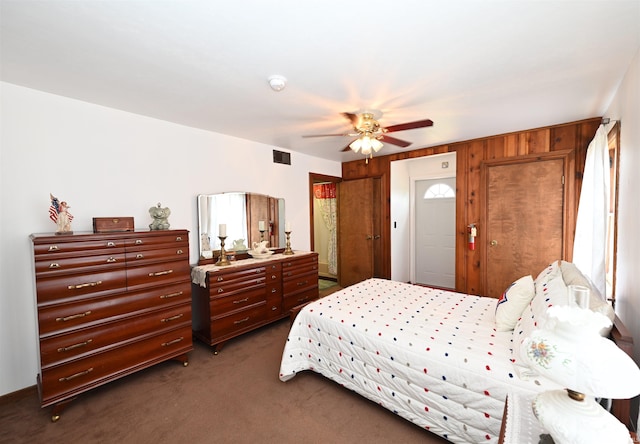 bedroom with wooden walls, ceiling fan, and carpet