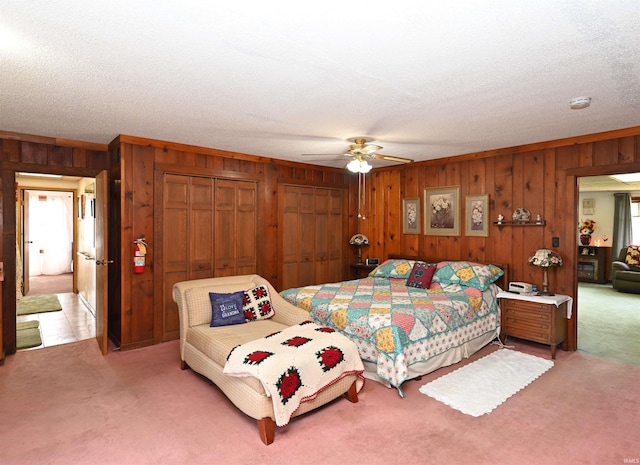 carpeted bedroom featuring ceiling fan, multiple closets, a textured ceiling, and wooden walls