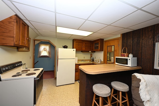 kitchen featuring a kitchen breakfast bar, sink, a paneled ceiling, and white appliances