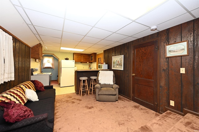 living room featuring wood walls, a drop ceiling, washer / clothes dryer, and light carpet