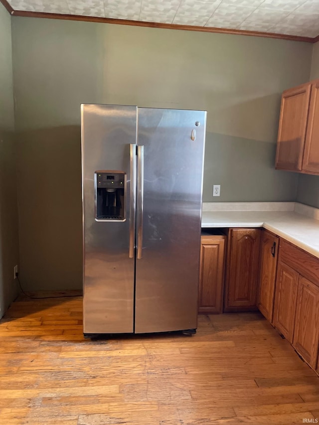 kitchen with light wood-type flooring, crown molding, and stainless steel fridge