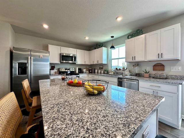 kitchen featuring white cabinets, a kitchen island, light stone countertops, and stainless steel appliances